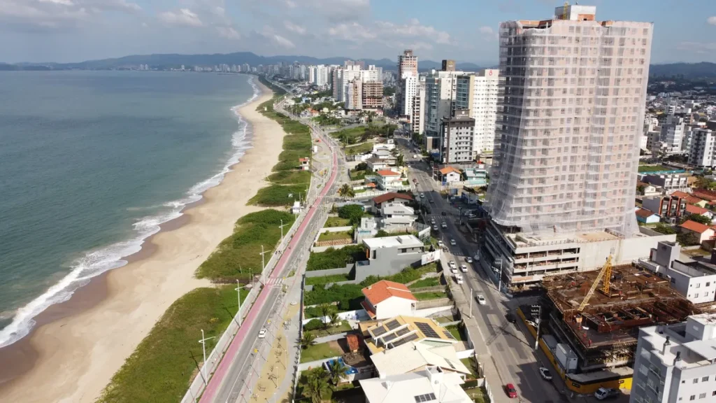 Vista aérea de Balneário Piçarras com prédios modernos à beira-mar ao pôr do sol.
