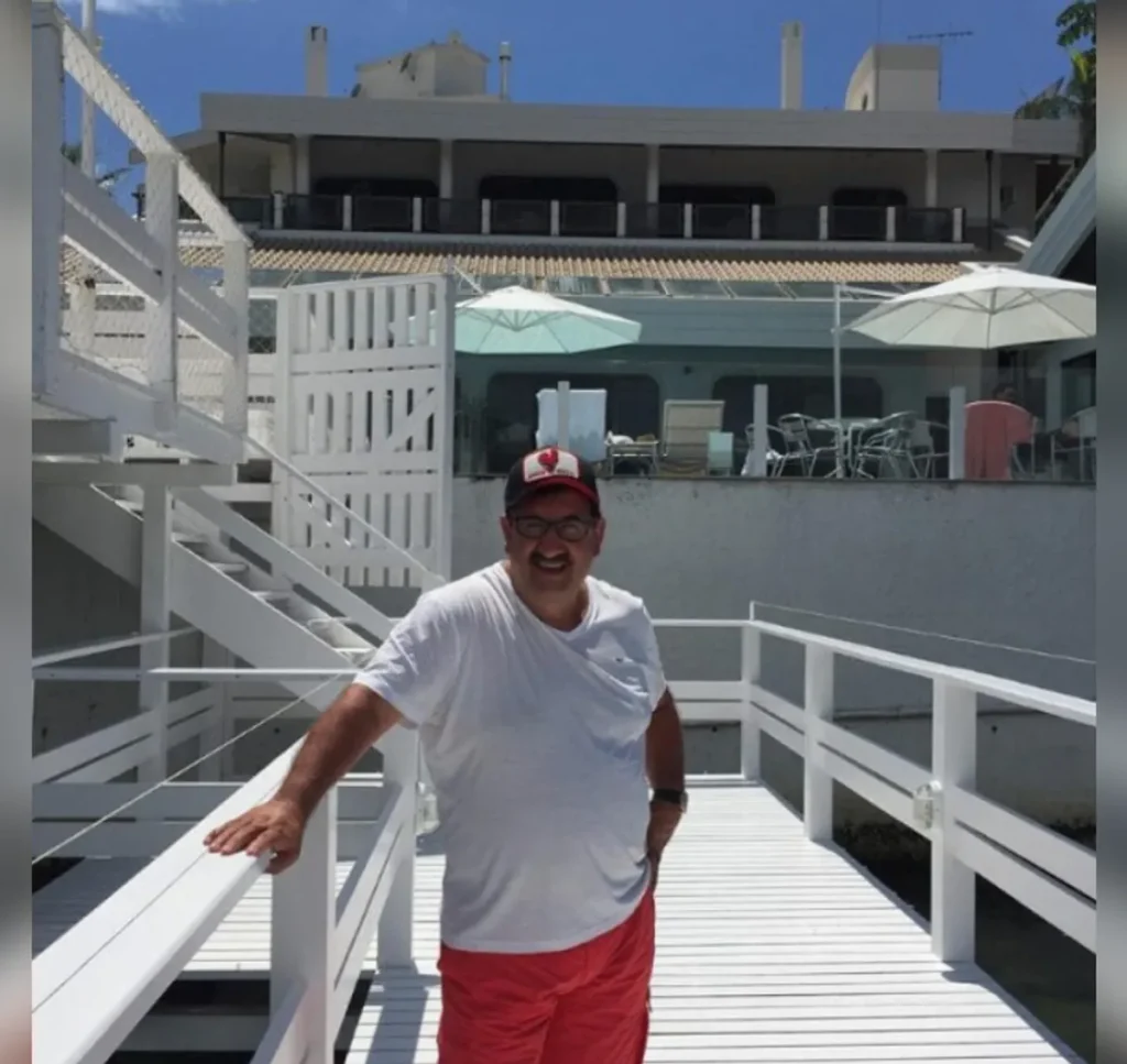 Ratinho, o apresentador, sorrindo em um luxuoso apartamento com vista para a praia de Itapema, mostrando sua confiança no mercado imobiliário local.