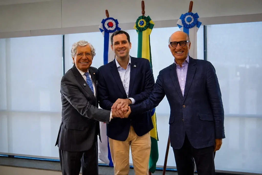 Executivos em evento de hotelaria no Rio de Janeiro discutindo investimentos com o logo BRAHIC ao fundo.