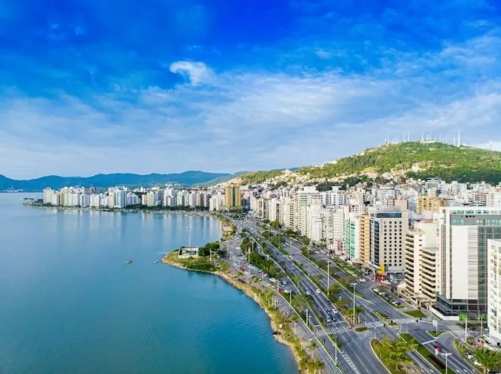 Paisagem urbana da Grande Florianópolis com destaque para a ponte Hercílio Luz iluminada ao entardecer, simbolizando o desenvolvimento e as oportunidades de moradia.