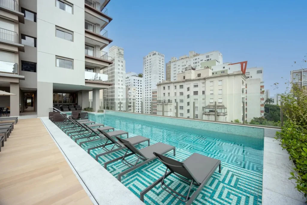 Lobby de empreendimento imobiliário de alto padrão integrando serviços de hotelaria, com recepção moderna e funcionário atendendo morador.